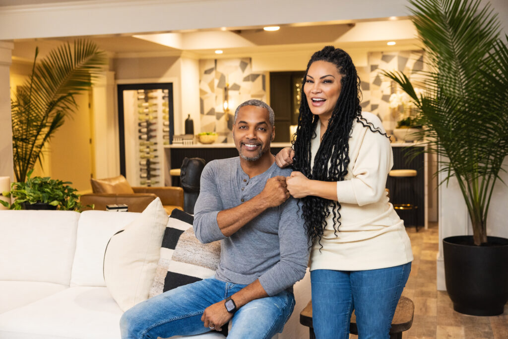 As seen on Married to Real Estate, hosts Mike Jackson and Egypt Sherrod pose for a photo in the newly renovated and designed basement bar and living area of their own home.