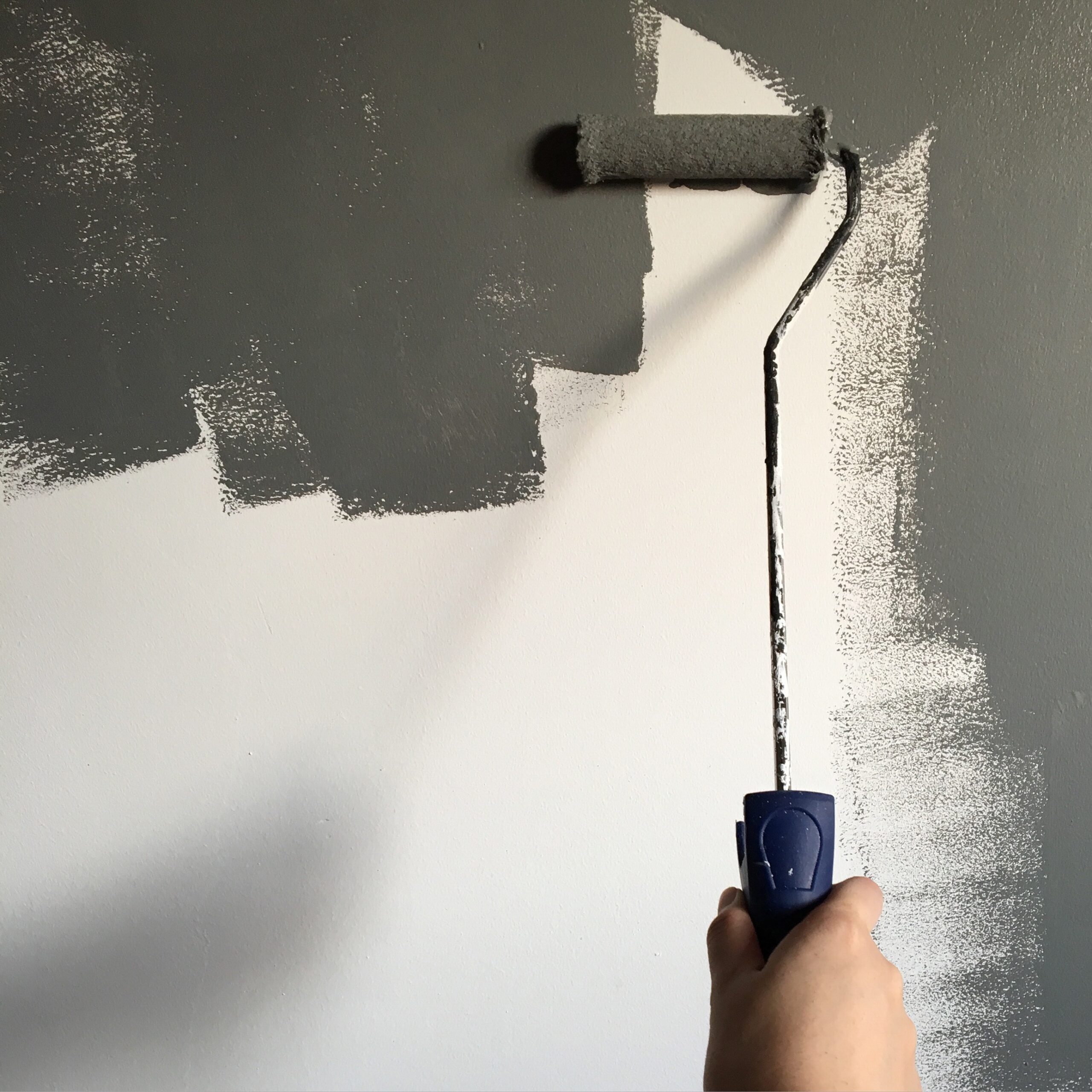 A hand holding a paint roller while performing interior painting.