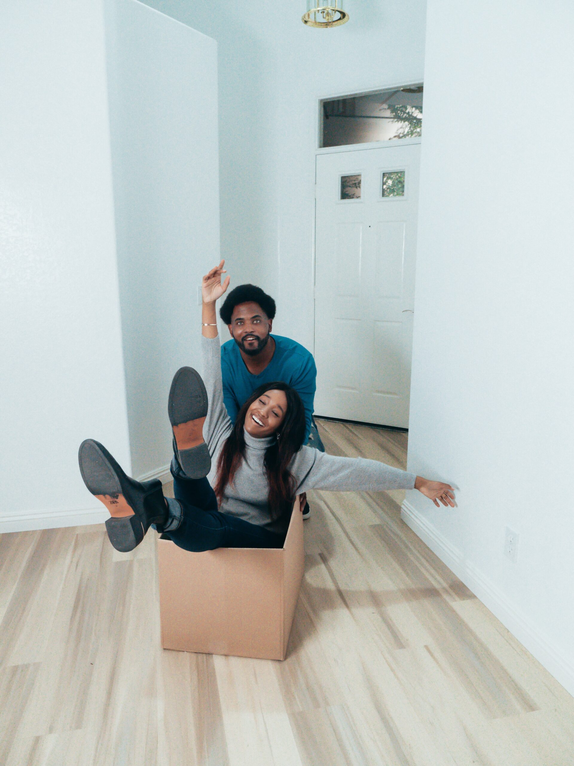 A man playfully pushing a woman sitting inside of cardboard box