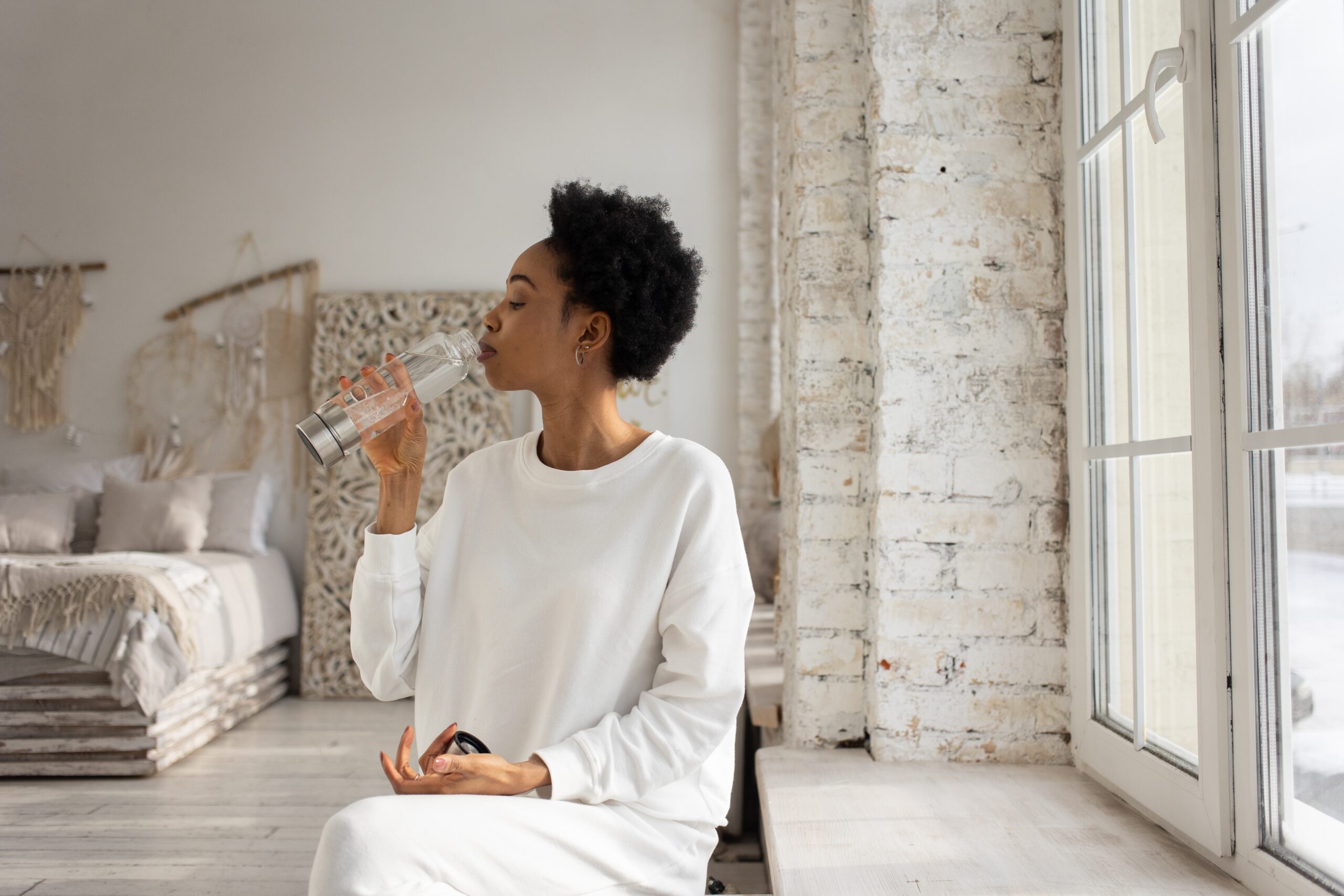 woman drinking out of a reusable water bottle in a beautiful home environment