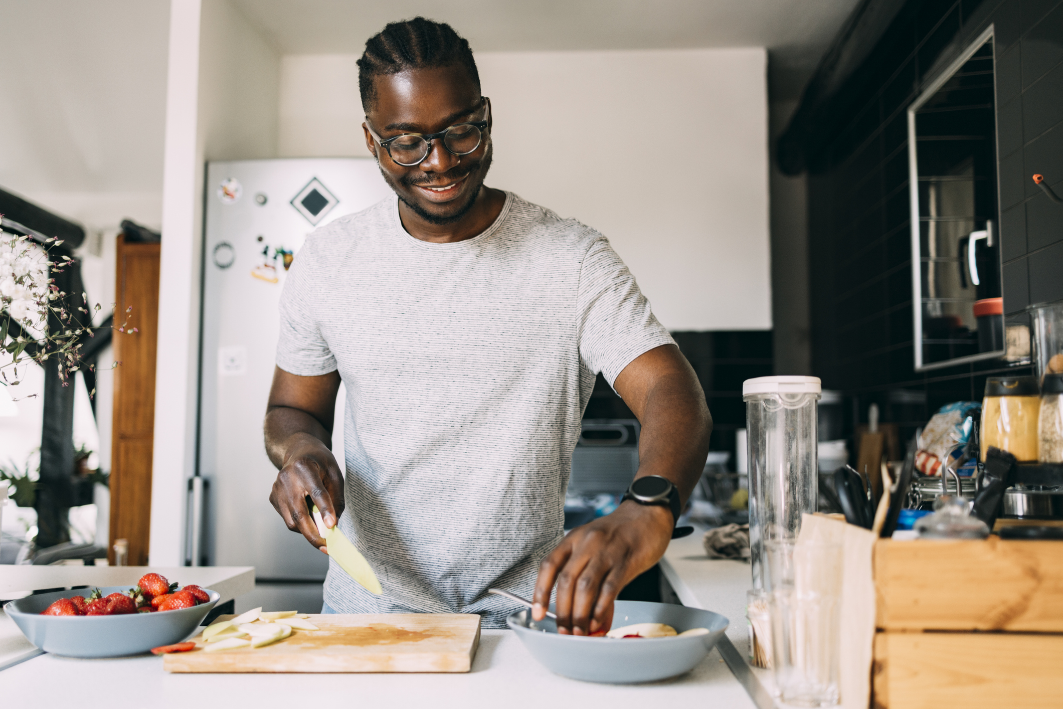 A smiling African-American male cutting fruit while making a healthy meal.