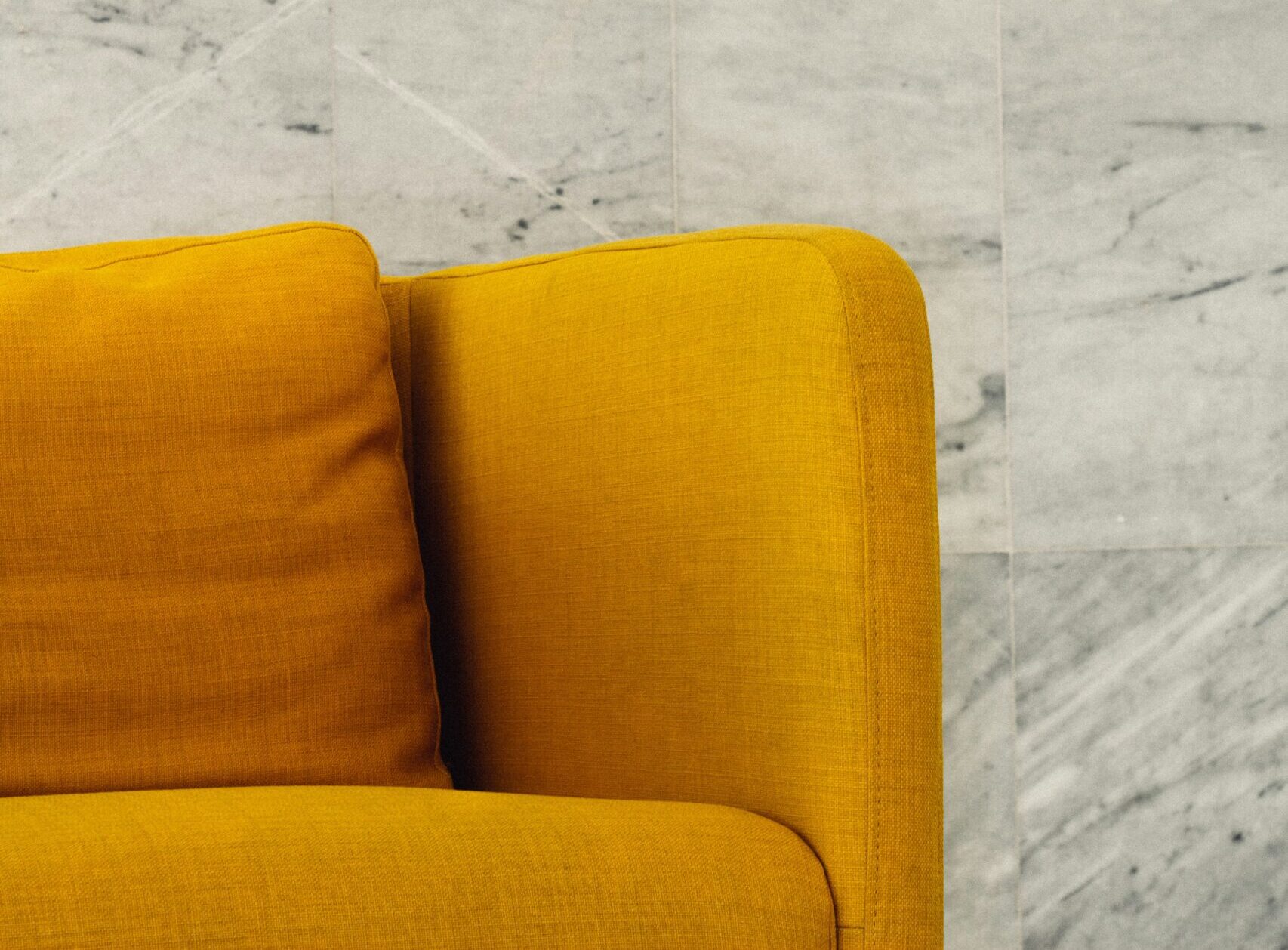 A mustard yellow couch in front of a white tile background.