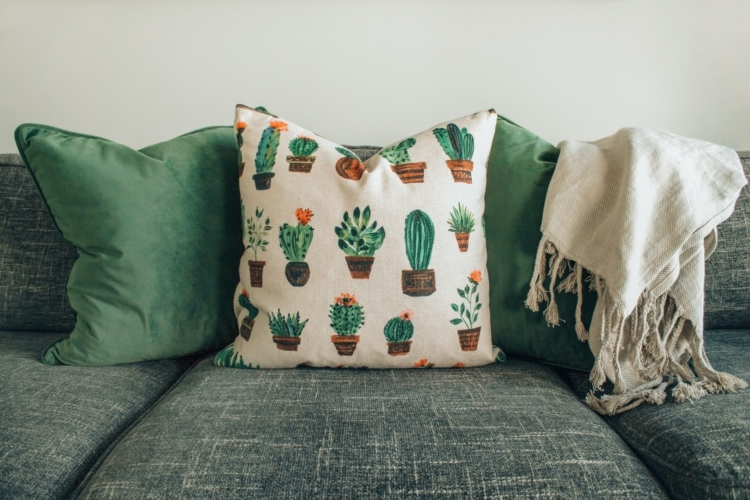A sage green couch with green and artsy pillows. Pictured: a couch with pillows.