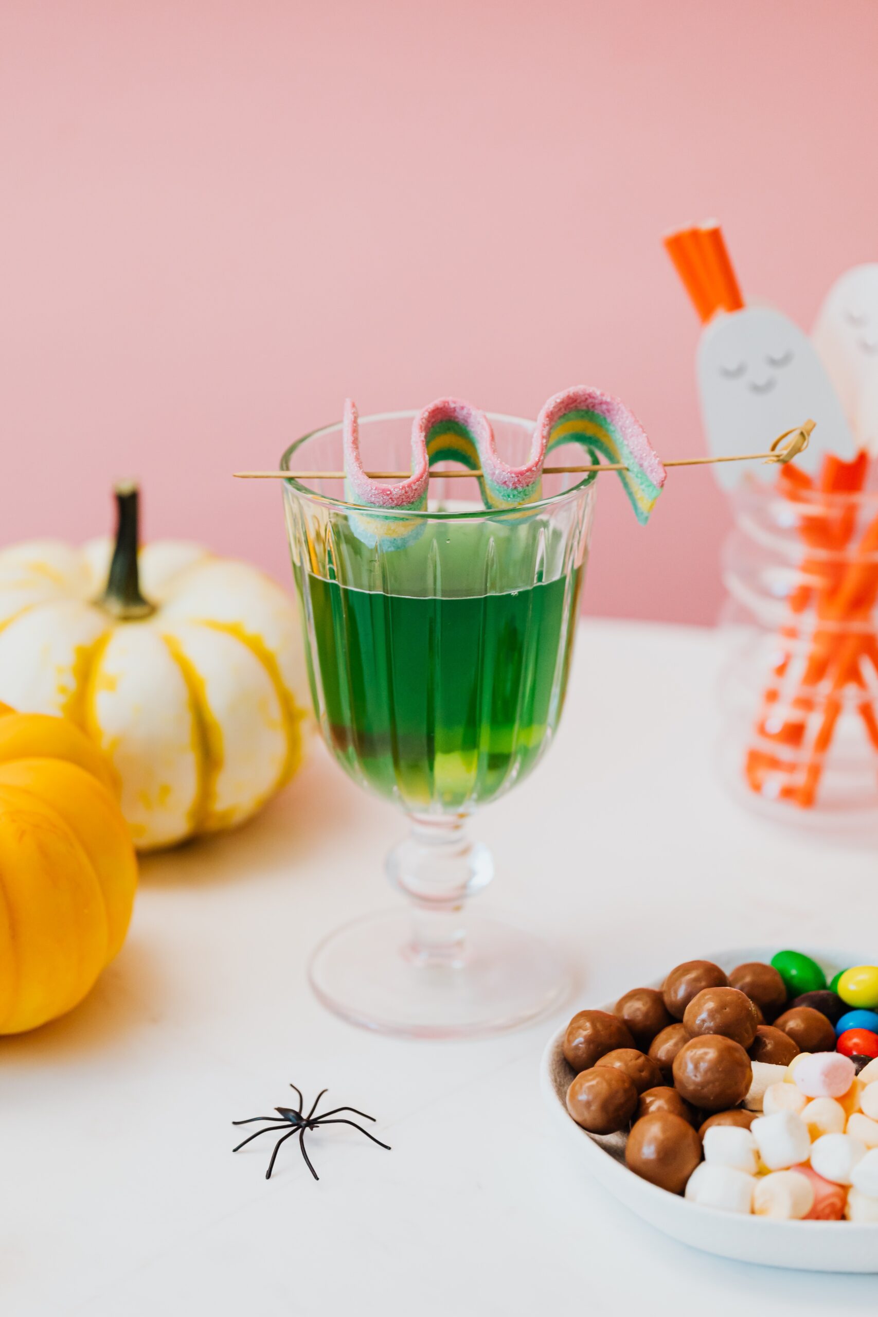 green halloween beverage with candy and pumpkins on table