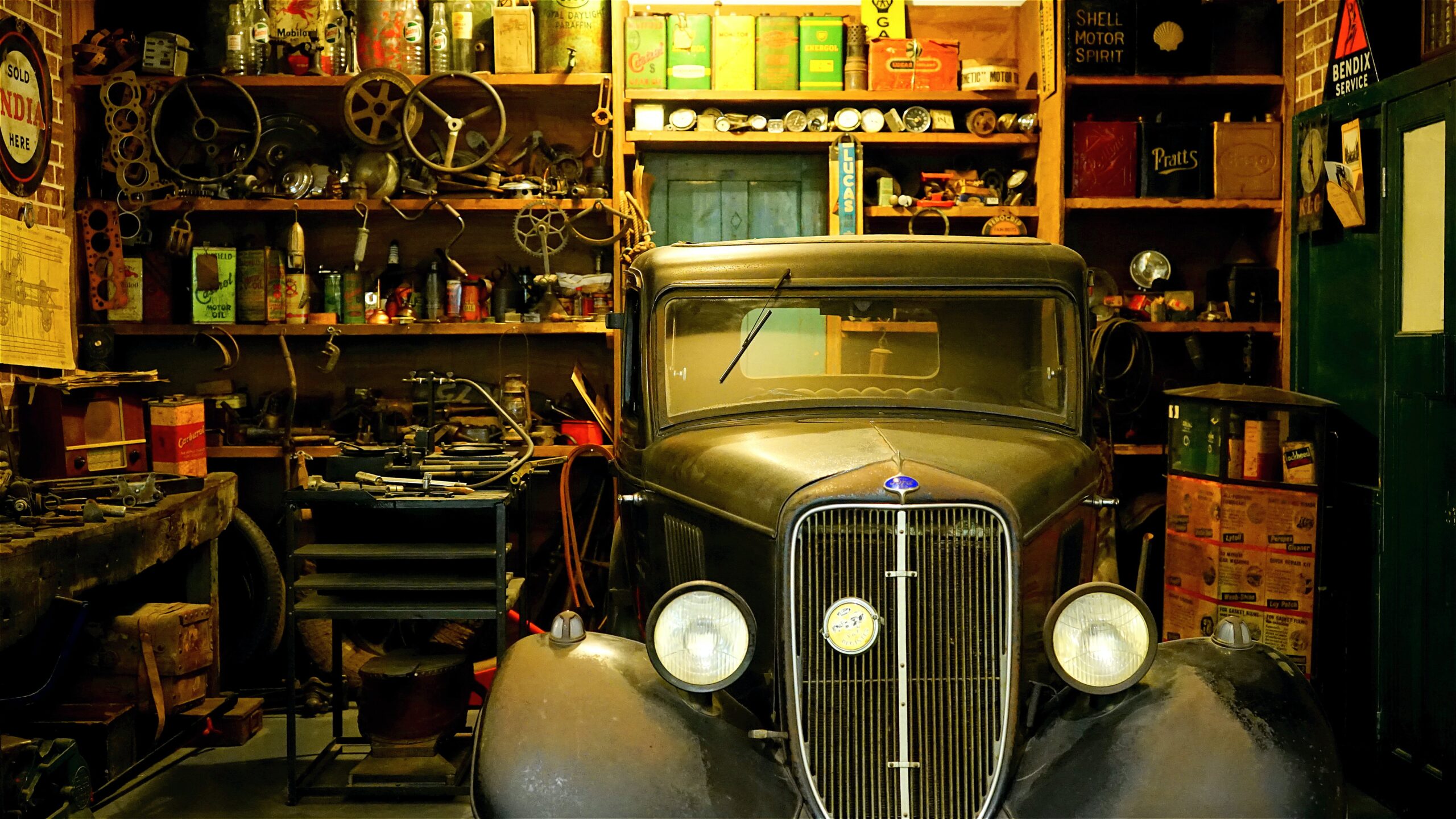 A messy garage with a vintage car parked inside