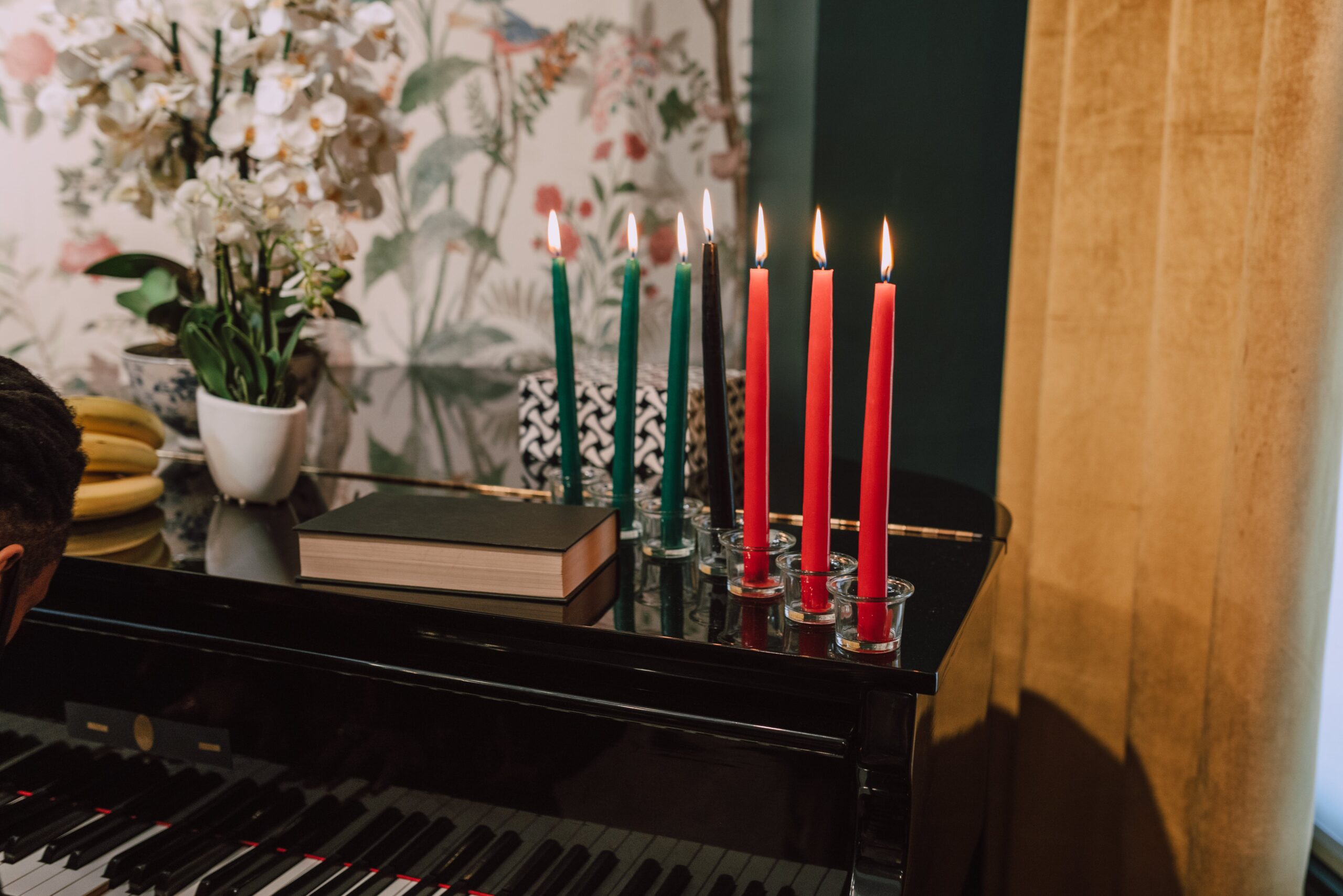 Use candles, throw pillows, blankets, vases, baskets and more in Kwanzaa colors to decorate your home this holiday season. Pictured: Kwanzaa candles on top of a piano.