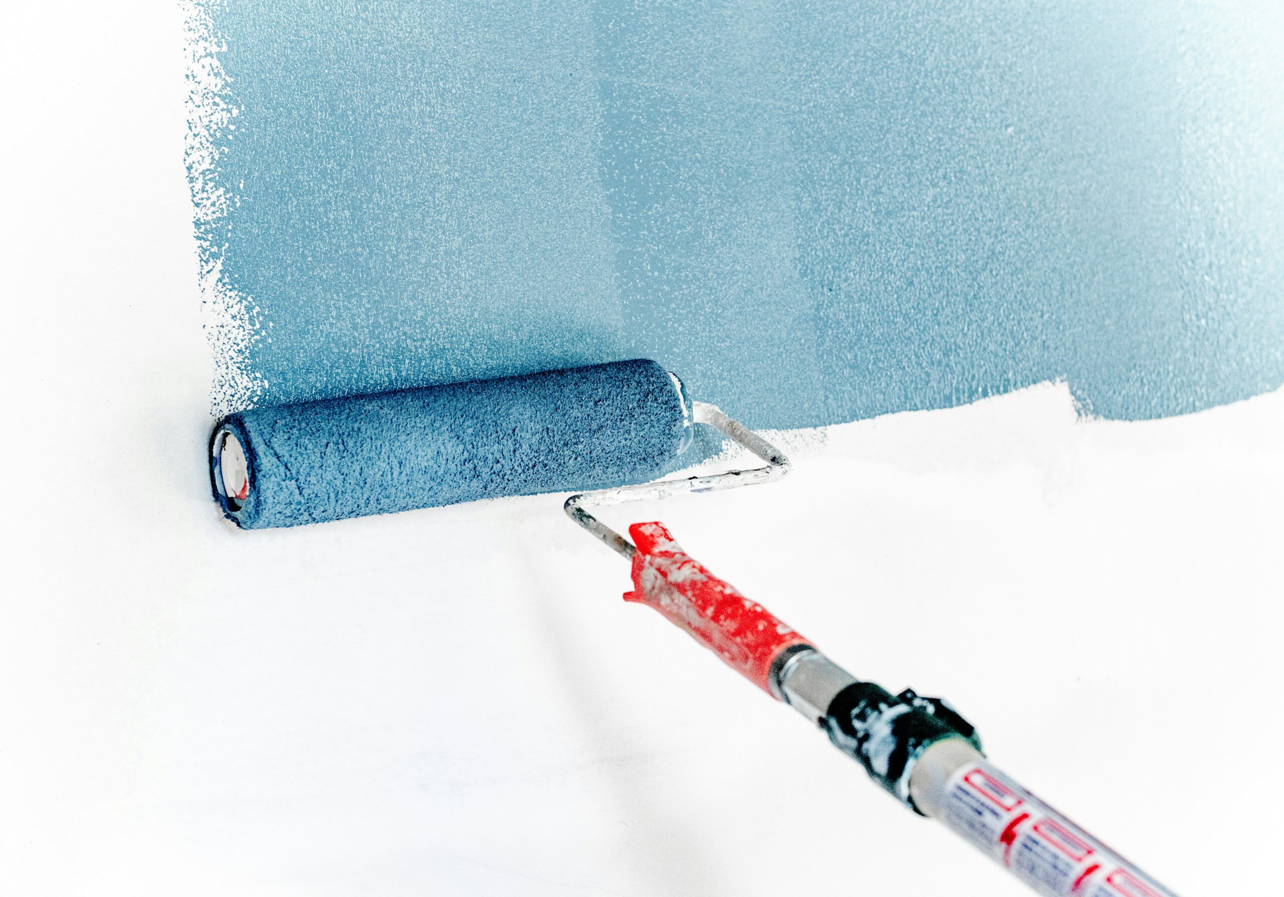 A paint roller rolling blue paint on a white wall