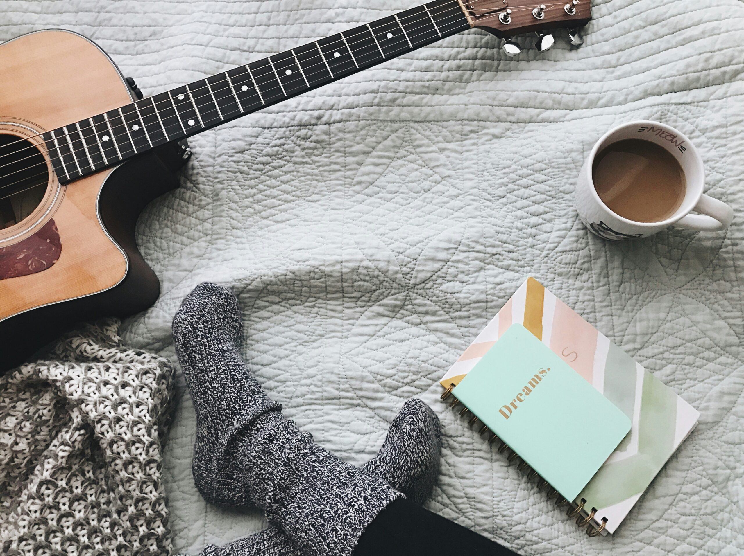 Here are a few ways to achieve the Tortured Poets Department aesthetic. Pictured: Someone sitting on a cozy bed with a guitar and journey