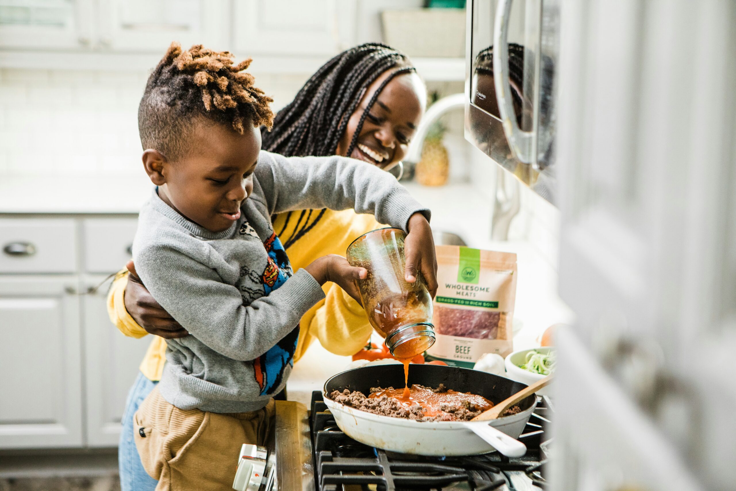 A young boy cooking with his mother in the kitchen