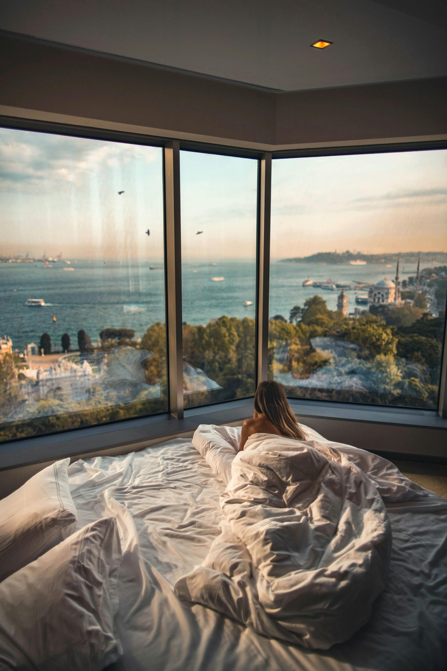 A woman laying down in bed looking out at a nice view