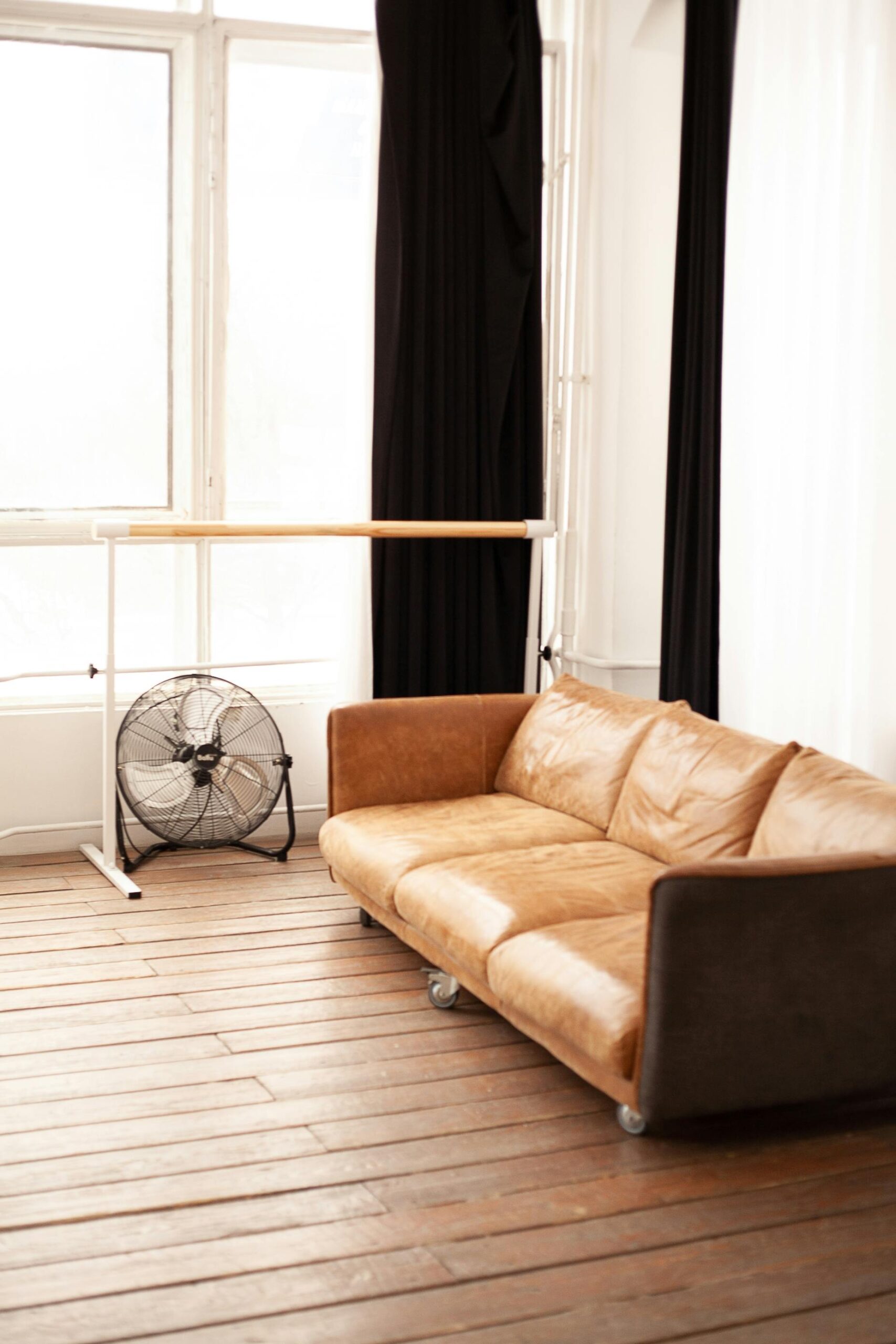 A floor fan next to a brown leather couch