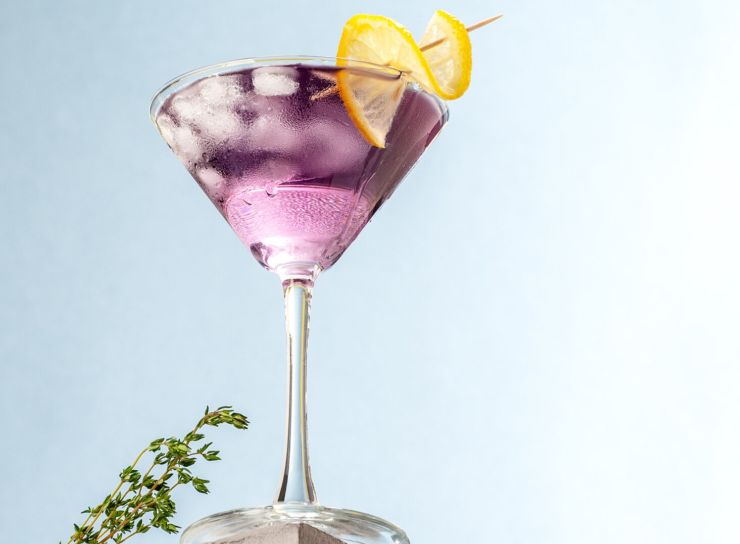 Cold cocktail with lavender syrup and lemon with ice on a light blue background.