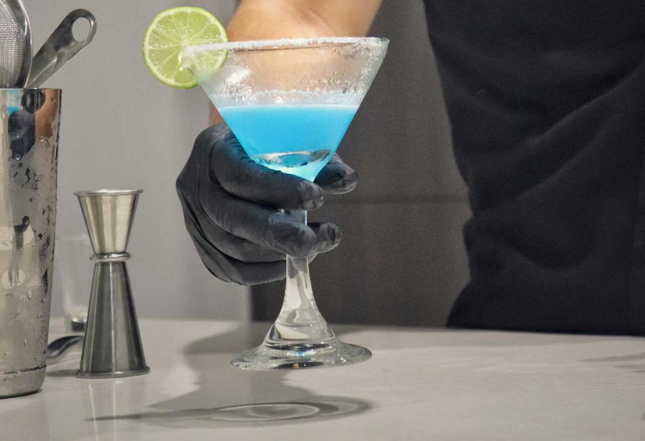 A Bartender Holding a Blue Cocktail with a Lime 