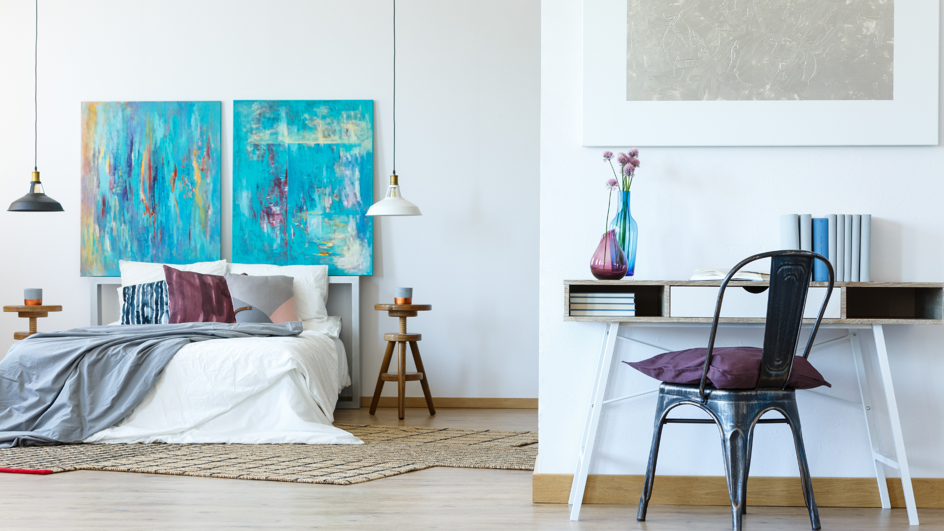 Large open white bedroom with desk, bed, night stands, blue canvas art and pendant lights