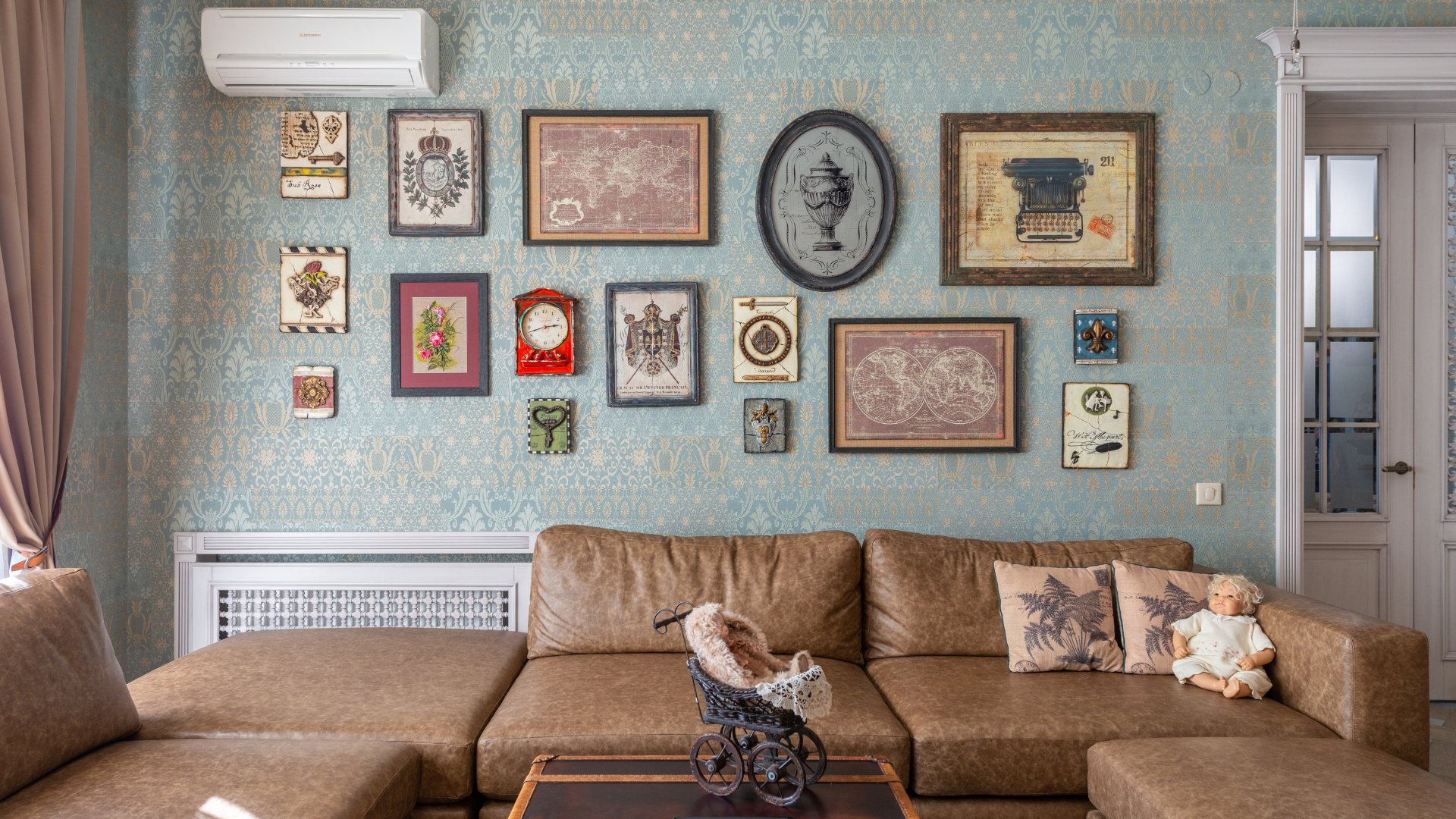 Living room with patterned wall paper, large leather sofa, and antique wall art, dolls and decor