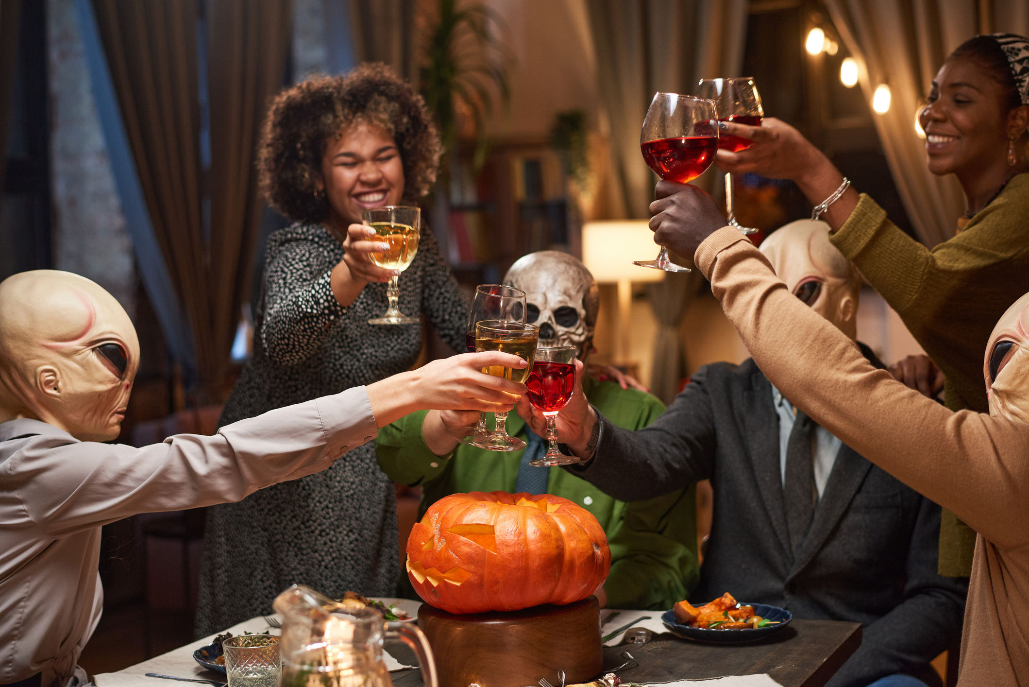 Group of of happy friends toasting with glasses of red wine and celebrating Halloween during home party