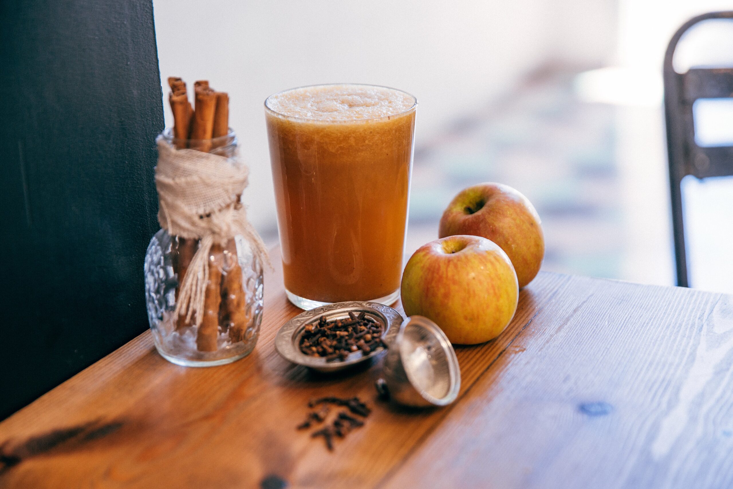 Image of an apple smoothie in a glass surrounded by apples and spices