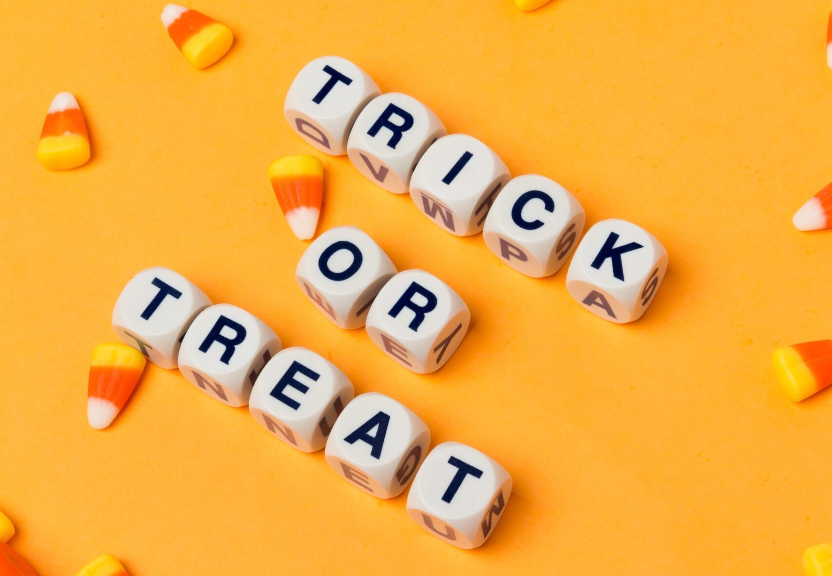 On an orange background, candy corn spews into the frame among letter dice that display trick or treat.