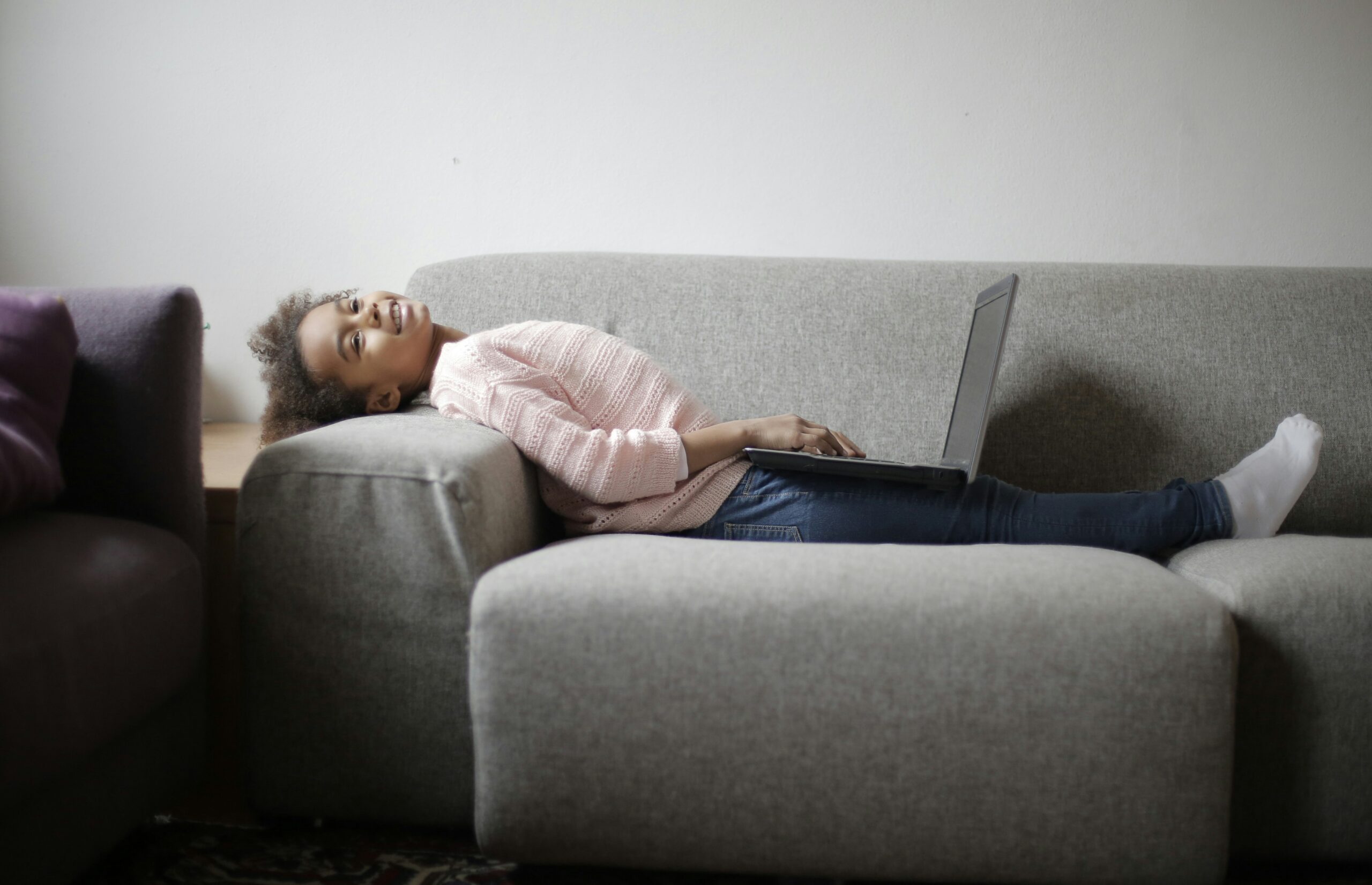 A young girl lounges on a plain gray, nearly featureless couch. 