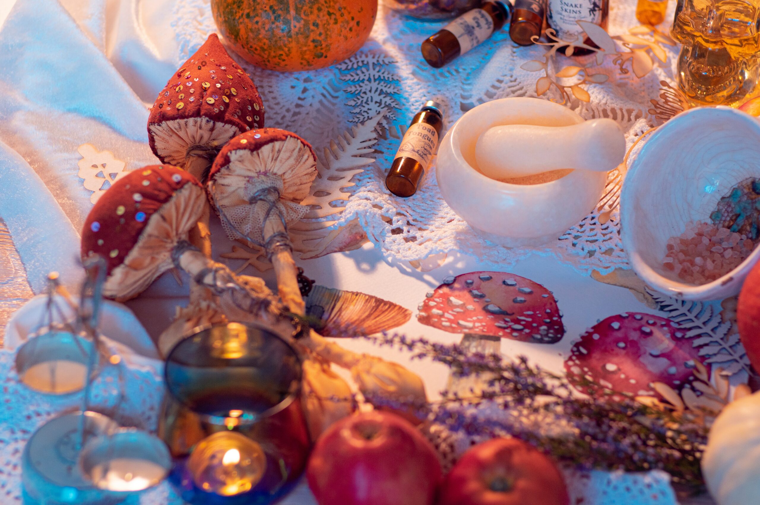 Fall apples, pumpkins and mushrooms, a white mortar and pestle, and jars of essential oils rest a white tablecloth. 