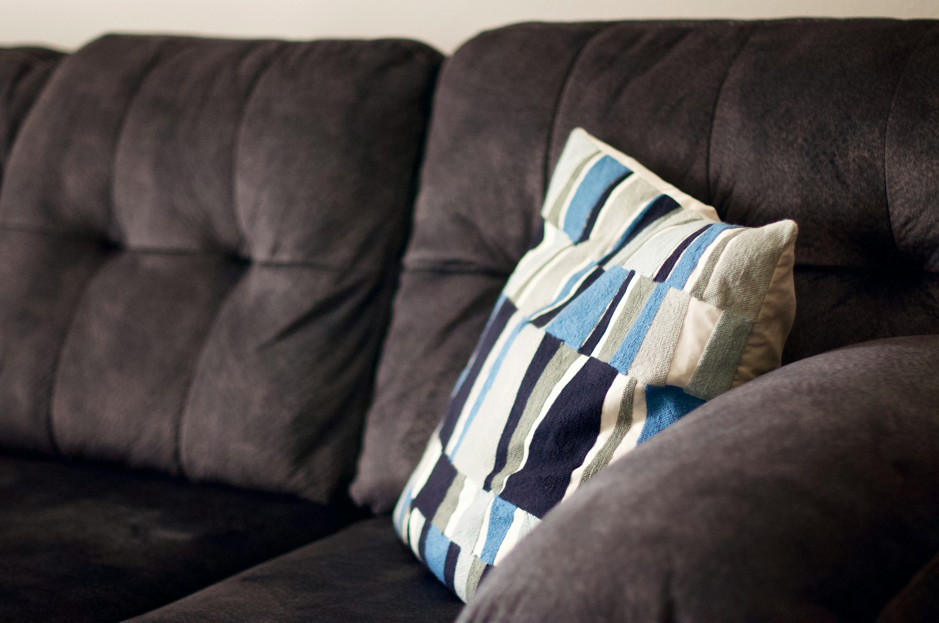 Brown suede couch with white, blue and tan couch pillow