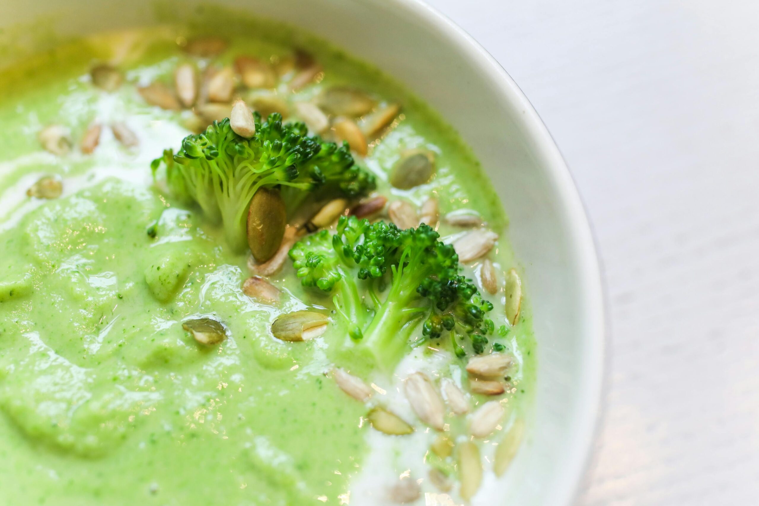 broccoli and potato soup in a bowl garnished with broccoli and seeds