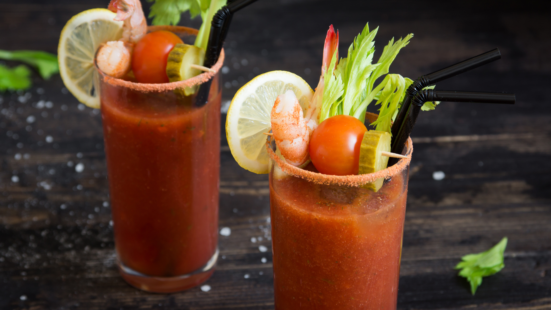 Bloody Mary brunch cocktails in glass with pickle tomato lettuce and shrimp garnish and salted rim on dark wooden background