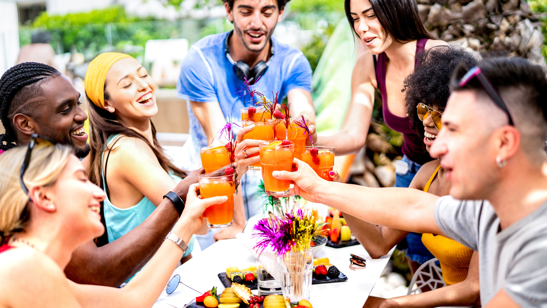 Group of friends clanking brunch cocktails at poolside party