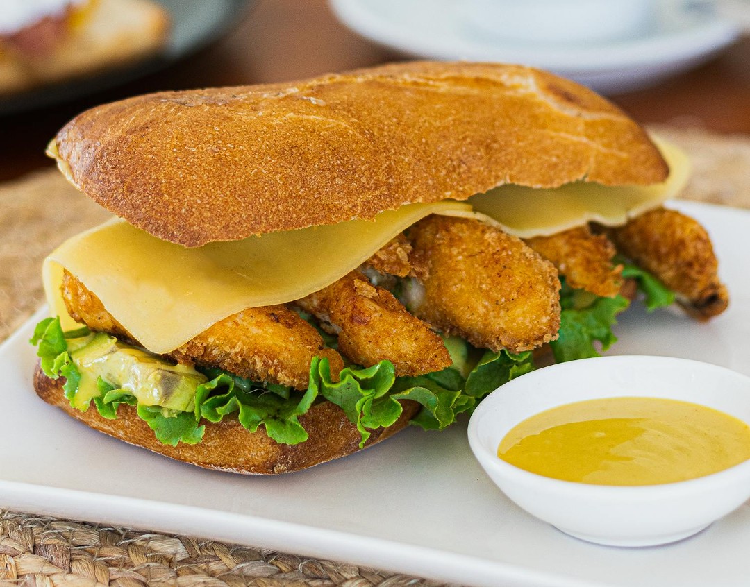 Fried seafood sandwich on a roll with mustard on the side