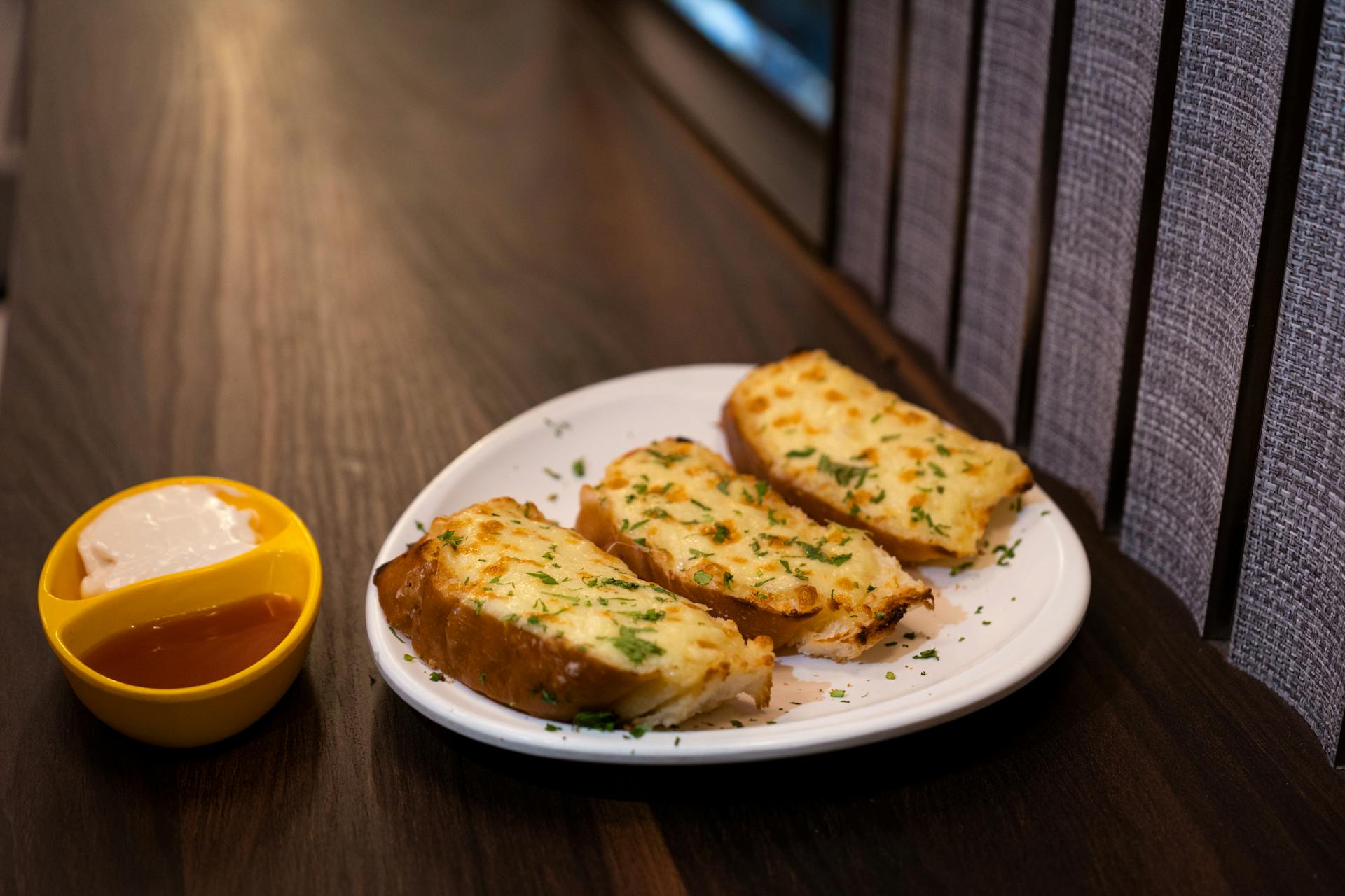 Garlic bread on a plate on top of a wooden table and butter in a yellow bowl