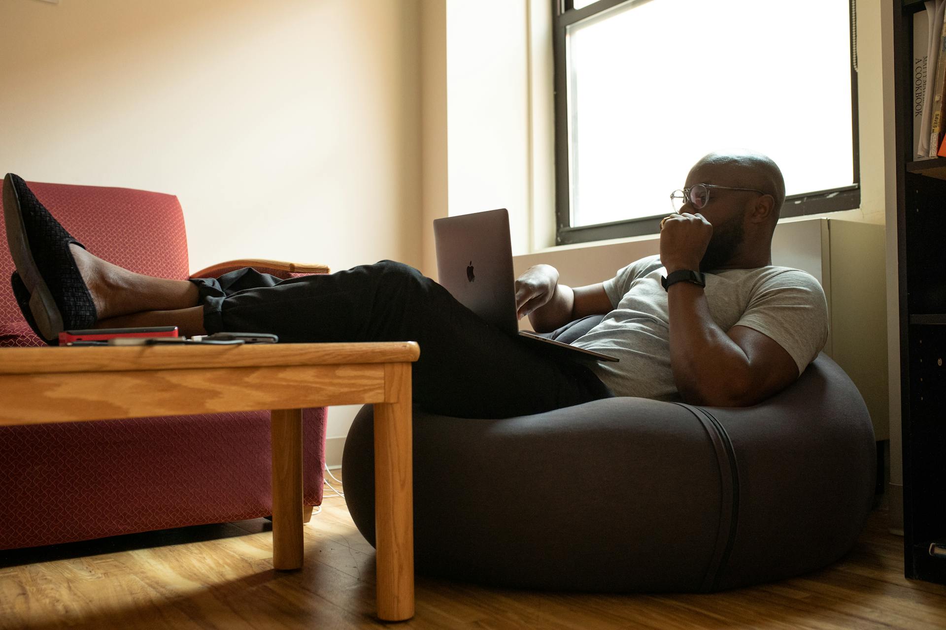 Man sits on bean bag chair while typing on laptop