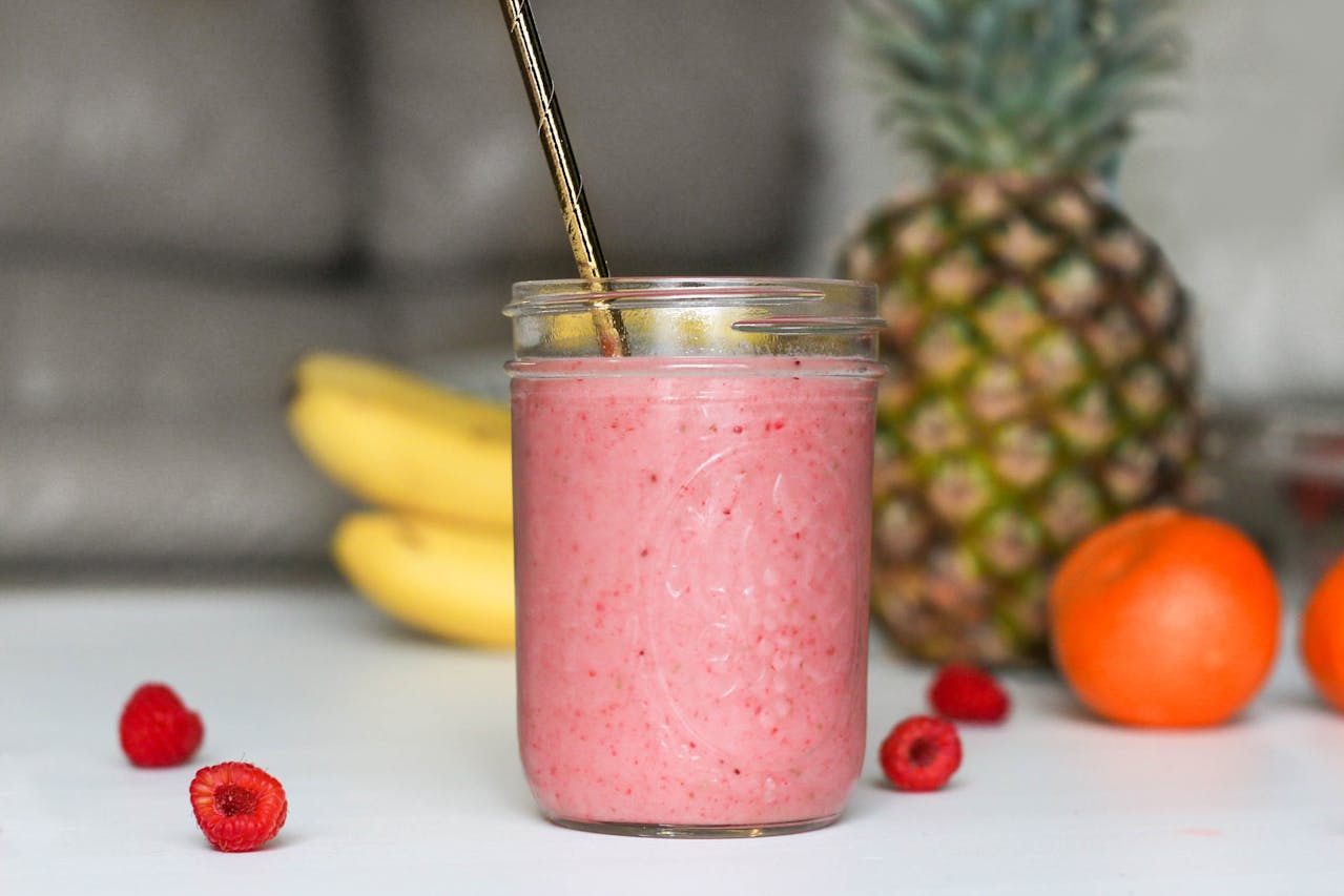 Strawberry smoothie with fresh fruit (bananas, pineapples, raspberries) in the background