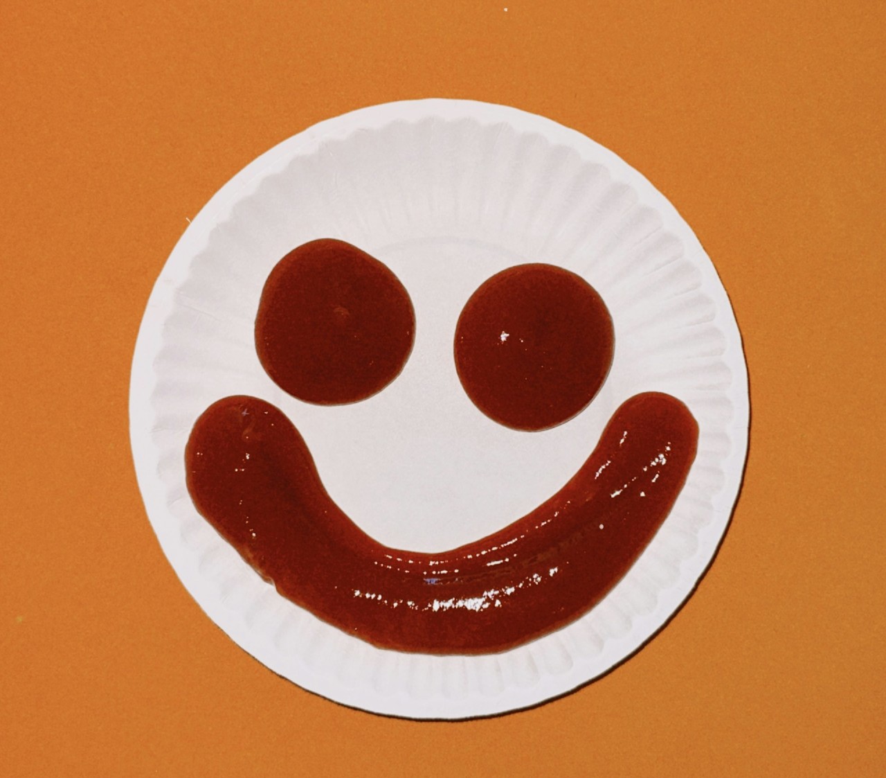 Ketchup squirted on a paper plate to make a happy face