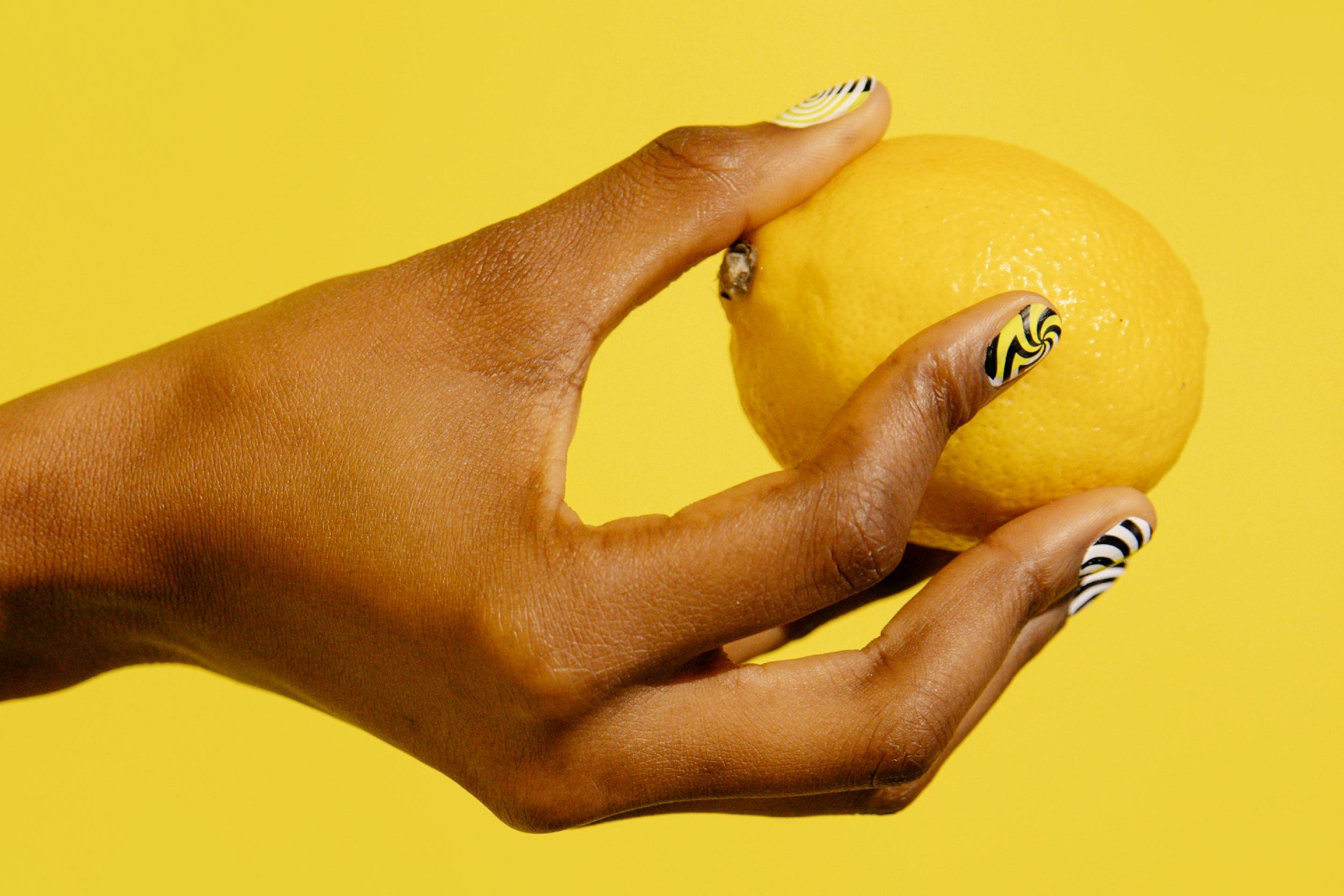 Hand with yellow, black and white manicured nails holding a lemon