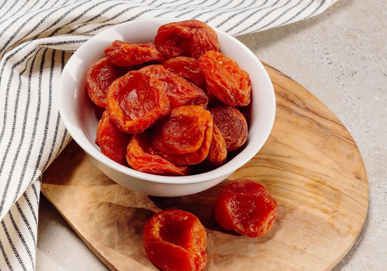 Dried apricot in a white bowl on top of a cutting board
