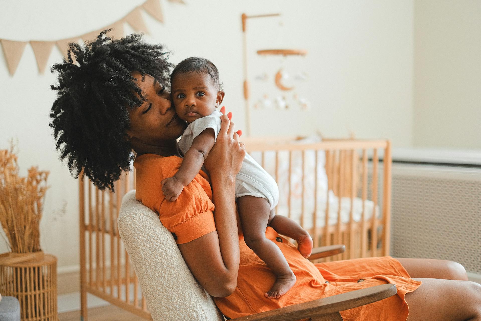Mother holds a baby while sitting in front of a baby crib